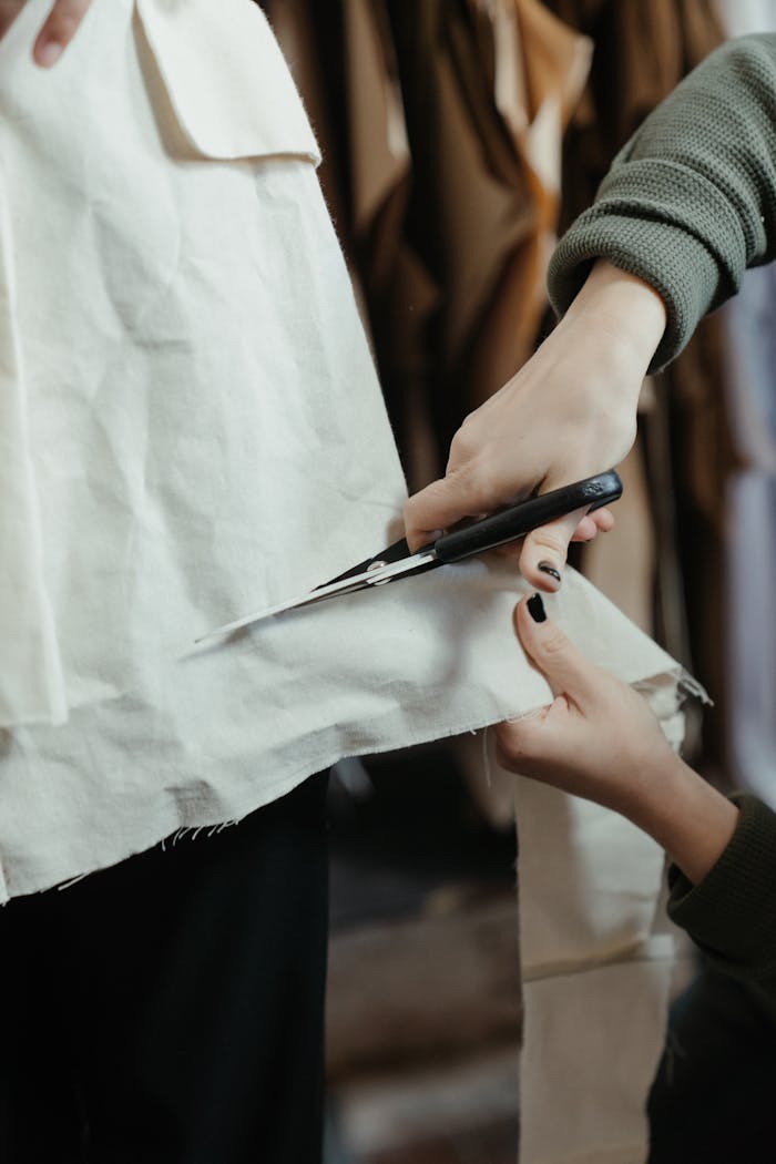 Hands cutting fabric with scissors in a clothing workshop, showcasing the art of tailoring.