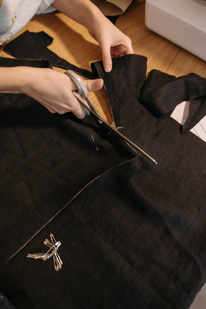 Hands skillfully cutting black fabric with scissors at a workspace.